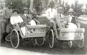 A pair of wheelchairs, their passengers, and the drivers, ca 1910s